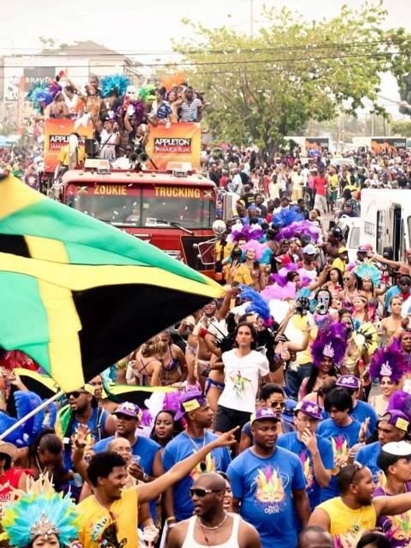 A vibrant Jamaican street parade with people waving the national flag and wearing colorful costumes.