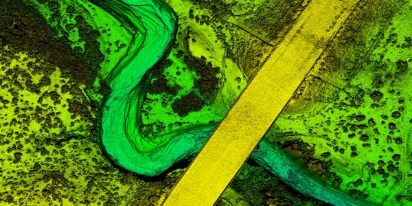 Aerial view of a green river winding under a yellow bridge.