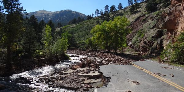 A damaged road next to a flowing stream in a mountainous area.