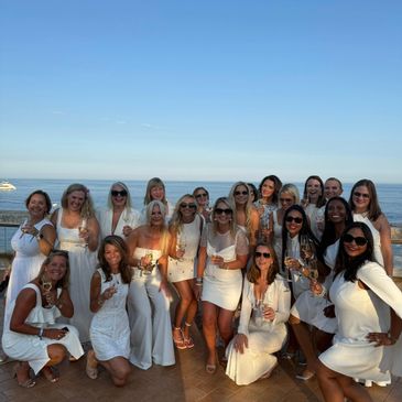 Group of women dressed in white posing by the seaside during sunset.