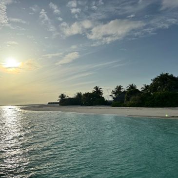Sunset over a tranquil beach with clear turquoise water and palm trees.