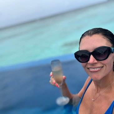 Woman in sunglasses holding a glass of champagne by the water.