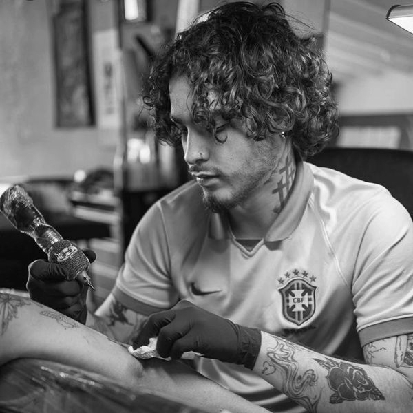 Tattoo artist focused on inking a client's arm, wearing gloves and a Brazil jersey.