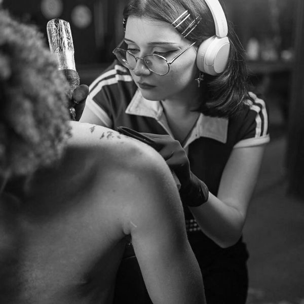 Focused tattoo artist wearing headphones and glasses inking a client's back.