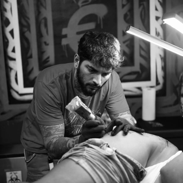 Tattoo artist focused on tattooing a client's leg in a studio.