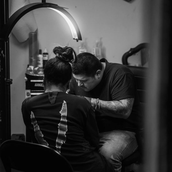 A tattoo artist focused on his work under a bright lamp in a studio.