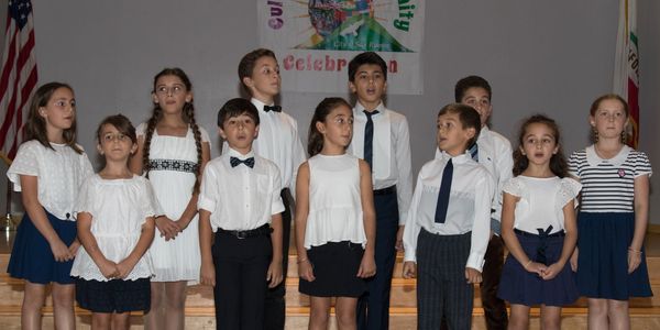 A group of children standing on stage, dressed formally, possibly singing.