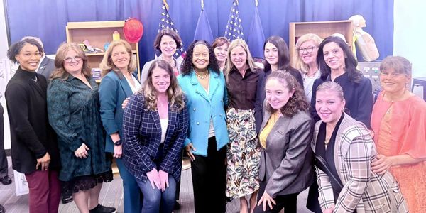 A group of women posing together indoors with flags in the background.