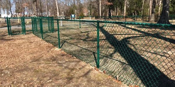 Green chain-link fence surrounding a park area with trees.