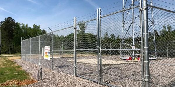 Chain-link fenced utility area with gravel and warning signs.