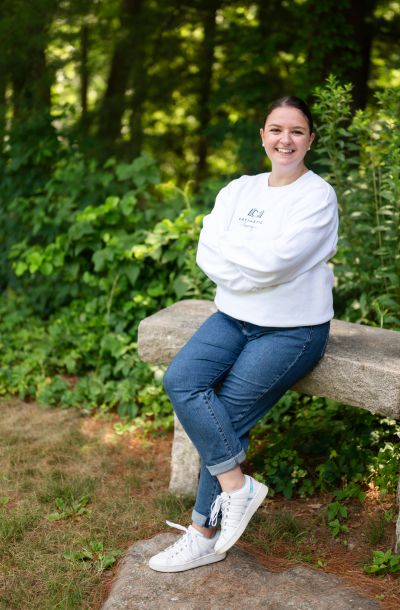 Young woman sitting on a stone bench in a lush garden.