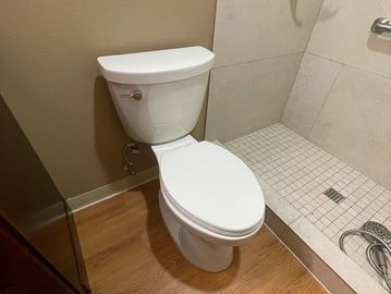 Clean white toilet next to a tiled shower area in a bathroom.