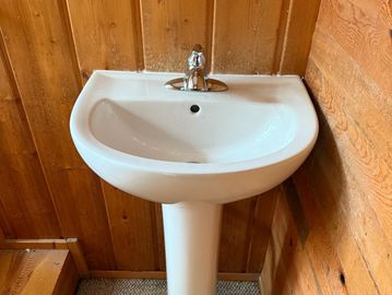 White pedestal sink against wooden wall panels in a rustic bathroom.