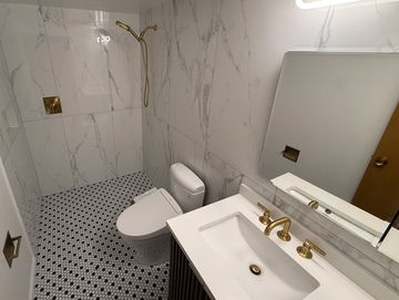 Modern bathroom with marble walls and gold fixtures.