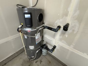 A modern water heater installed in a corner of a garage with insulated pipes.