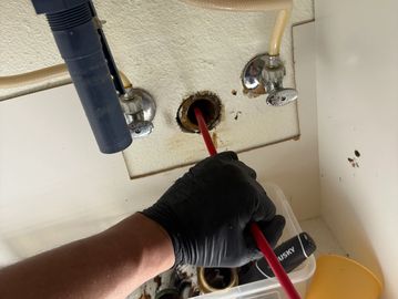 Technician using a drain snake to unclog a pipe under a sink.