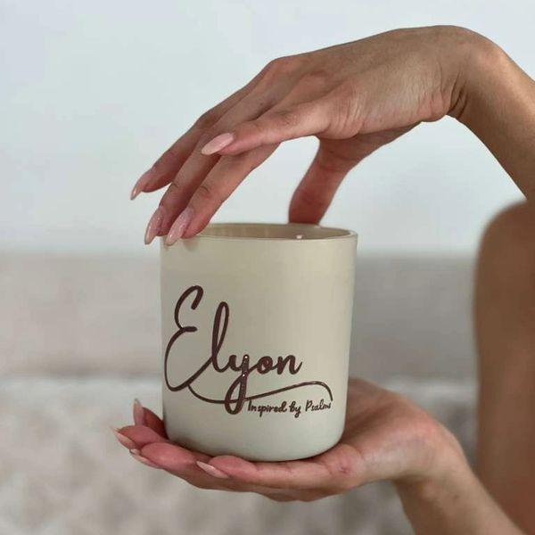 Hands with manicured nails holding a candle labeled 'Elyon Inspired by Psalms'.