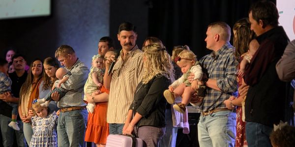 Group of adults holding babies on stage during an event.