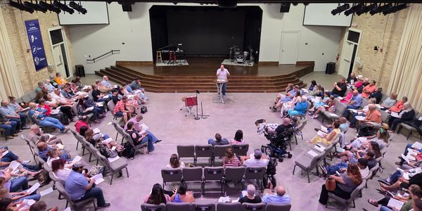 Speaker addresses a seated audience in a large room.