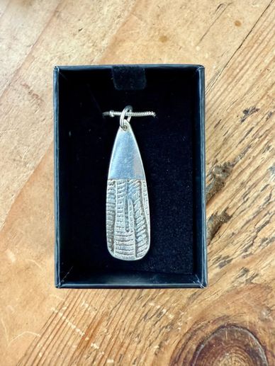 Silver pendant with textured design in a black box on wooden surface.