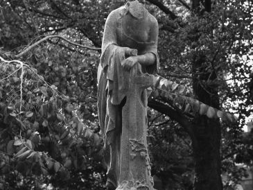 A headless statue standing among trees in a black and white photo.