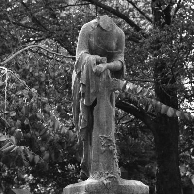 Headless statue draped in cloth in a forest.