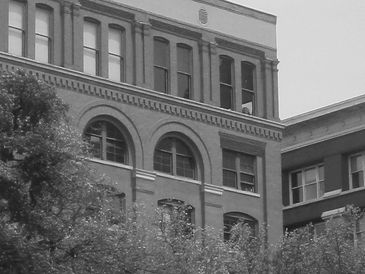 Black and white photo of a multi-story brick building with arched windows.
