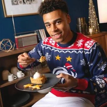 Joven sonriendo con suéter navideño mientras sostiene un plato con pastel.