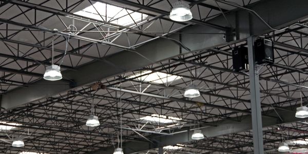 Industrial warehouse ceiling with numerous hanging lights and skylights.