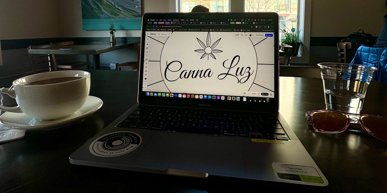 Laptop with 'Canna Luz' on screen in a cozy cafe.