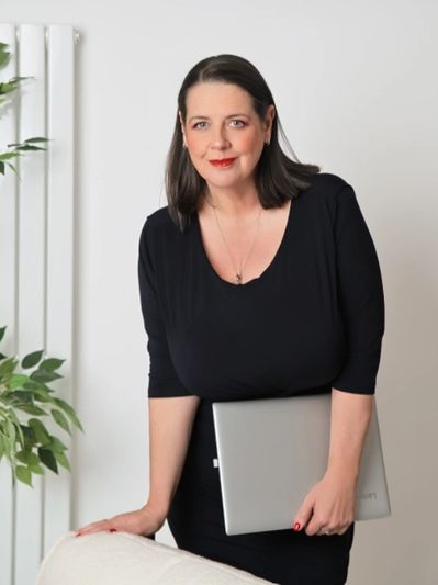 Professional woman in black holding a laptop, posing confidently indoors.