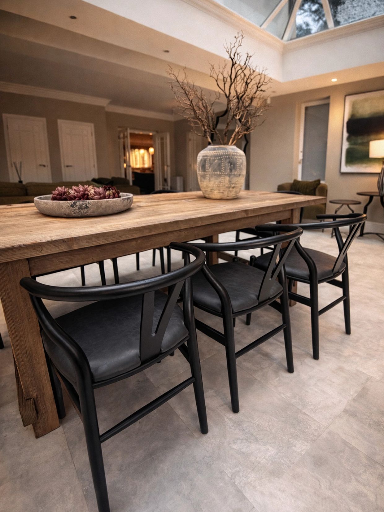 Modern dining room with wooden table and black chairs under skylight.