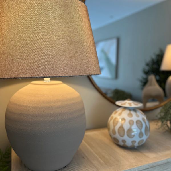 A beige table lamp with a textured shade on a wooden surface.