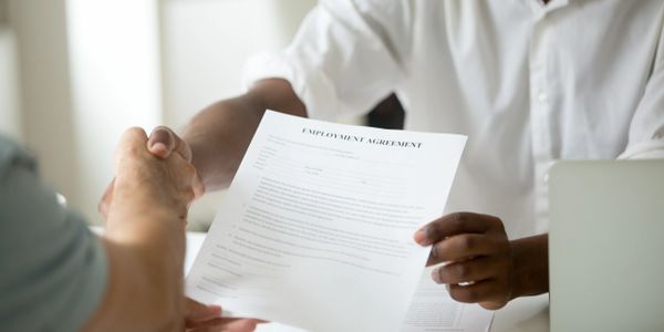 Two individuals shaking hands over an employment agreement document.