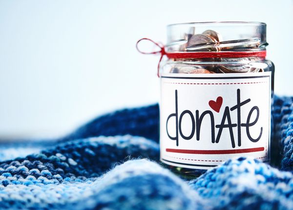 A glass jar labeled "donate" with a red heart filled with coins, resting on a blue, textured blanket