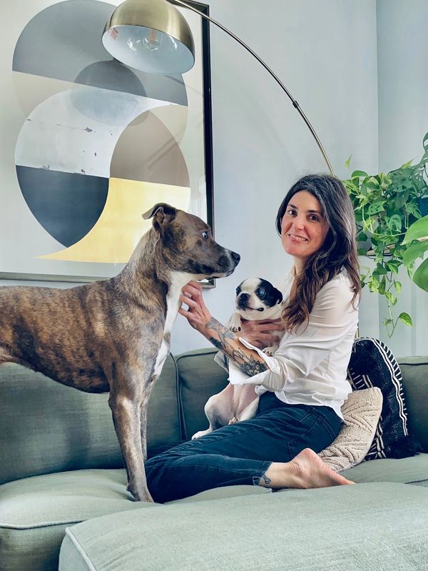 Woman sitting on couch with two dogs, smiling.