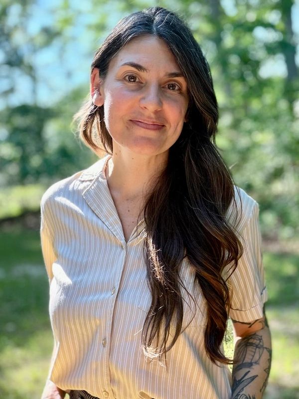 Woman with long dark hair smiling outdoors in striped shirt.