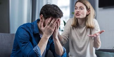 Woman angrily speaking to a man with his head in his hands