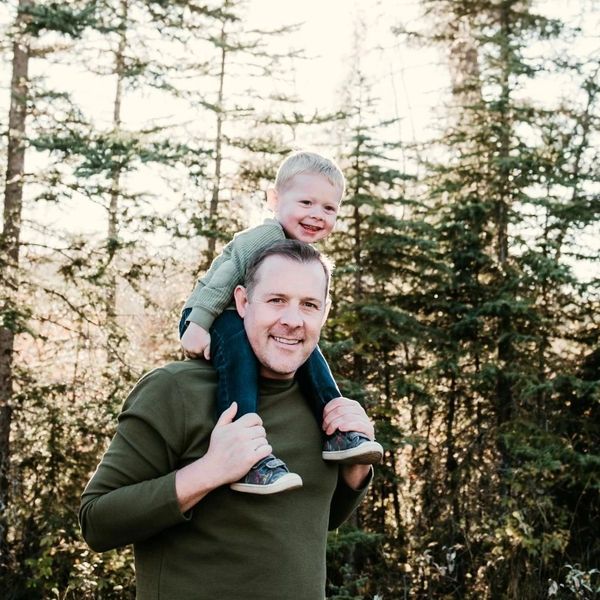 Father gives son a piggyback ride in a sunlit forest.