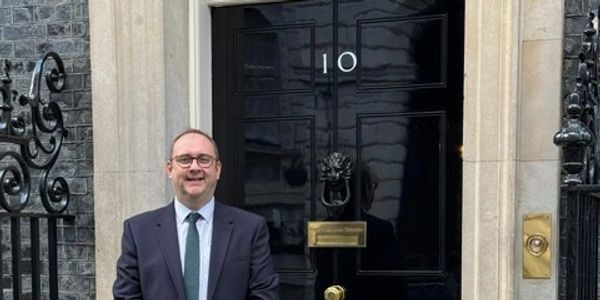 Man in suit standing in front of 10 Downing Street door.