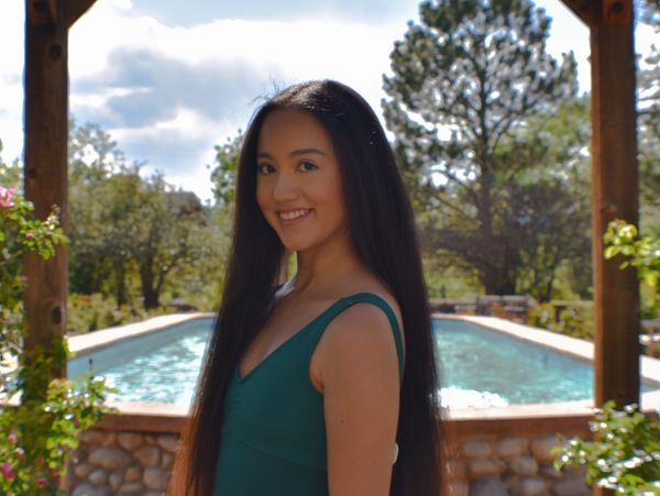 Young woman in teal dress smiling by pool.