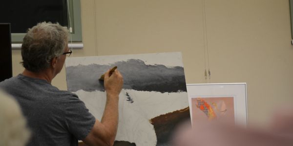 An artist painting a snowy landscape on canvas indoors.