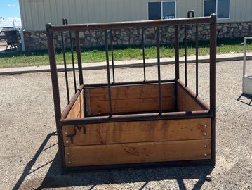 Empty wooden and metal livestock feeder in an outdoor area.