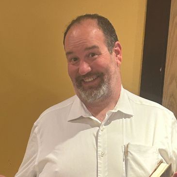 Smiling man in white shirt holding a book.