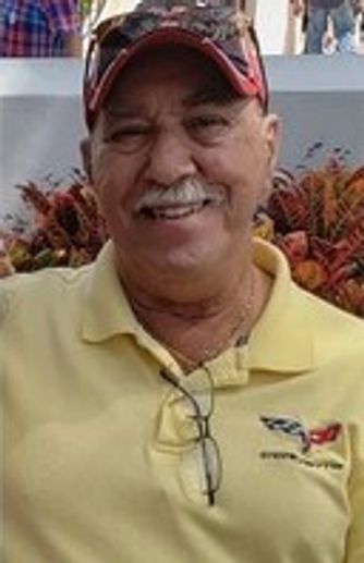 Smiling man in yellow polo and cap with glasses hanging from his shirt.