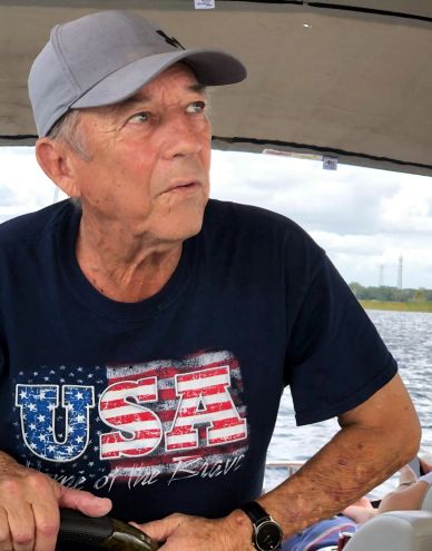 Older man wearing a USA shirt and gray cap on a boat.