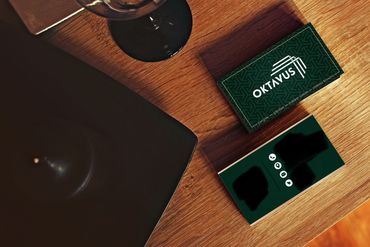 Elegant business cards for Oktavus on a wooden table with a black candle and glass.
