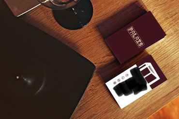 Business cards on a wooden table beside a black plate and a wine glass.