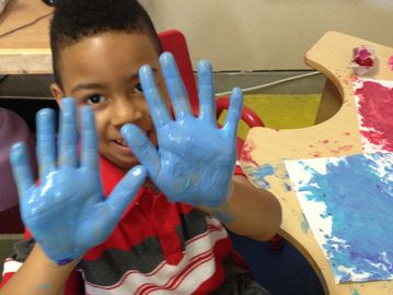 Child showing hands covered in blue paint with a joyful expression.