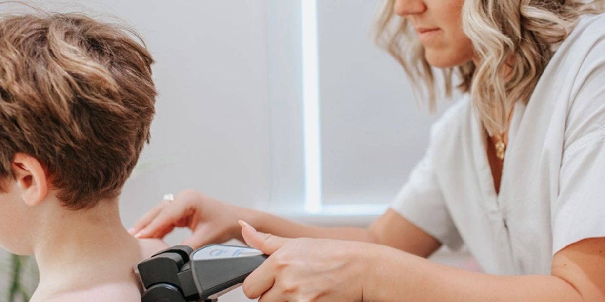 A woman uses a device on a child's back, possibly for medical or therapeutic purposes.